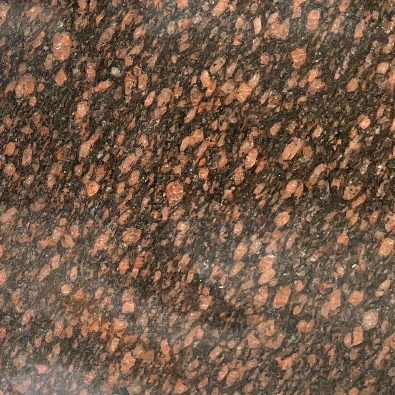 A close-up image of Tan Brown granite, featuring a dark brown to black background with prominent reddish-brown and tan mineral flecks and crystals. This detailed stone texture showcases the natural beauty and durability of the material, ideal for memorial designs.