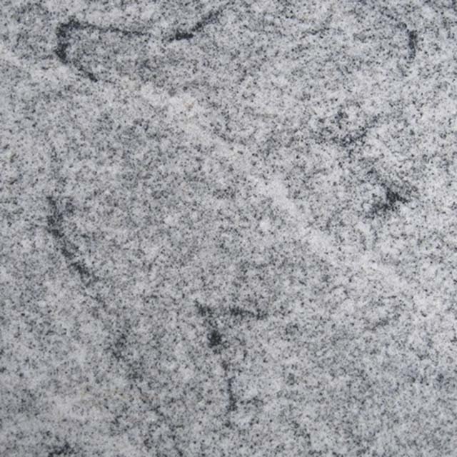 A close-up image showing the natural speckled texture of light grey granite stone, commonly used for headstones and memorials. It features a mix of white, grey, and black flecks, illustrating the durable and rustic surface of the material.